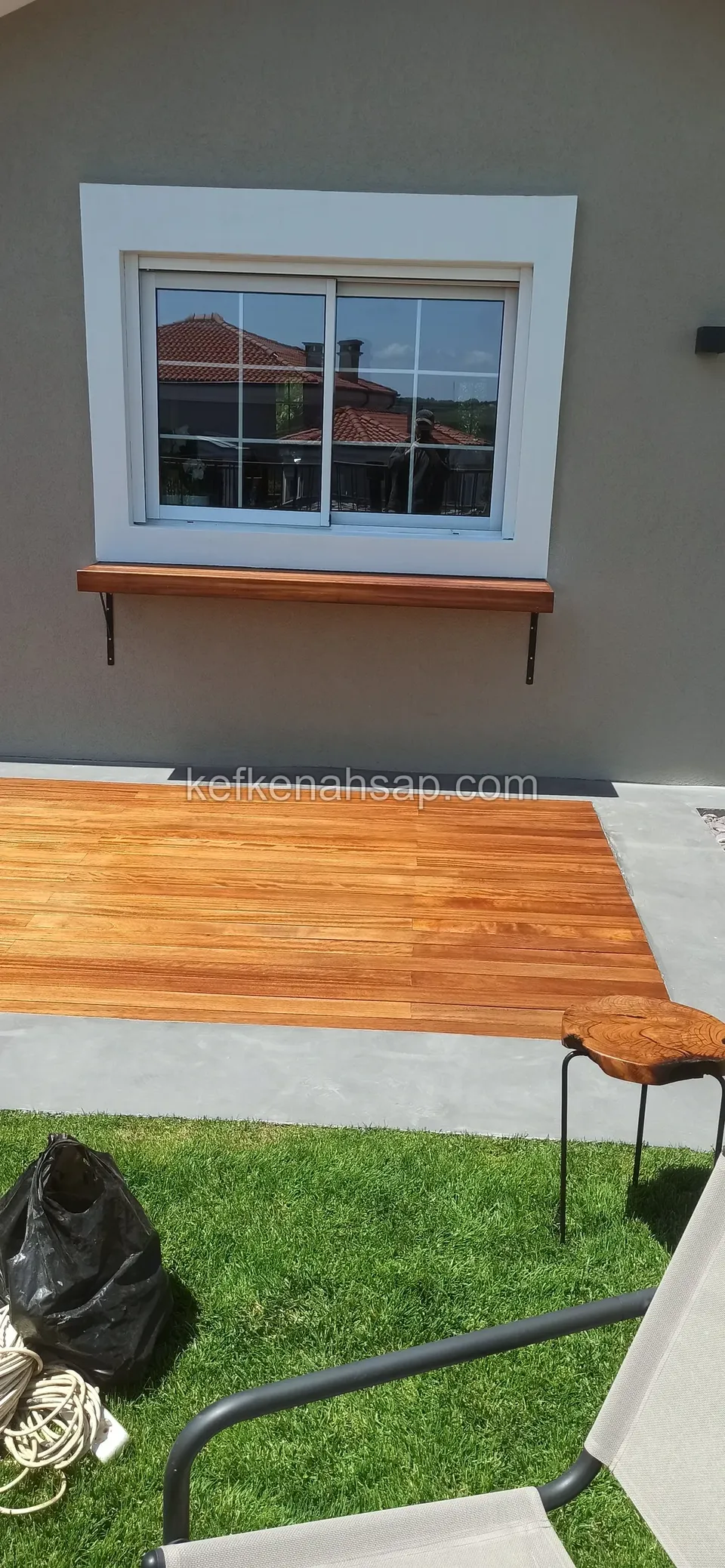 Honey-toned varnished deck laid beside a grey surface, in front of a timber shelf under a window