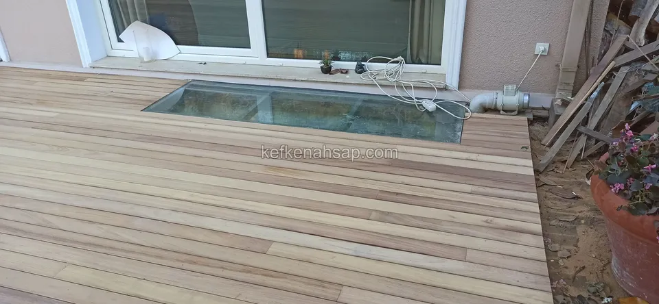 Pencere altındaki cam kapaklı havalandırma boşluğunun etrafına döşenmiş açık renkli deck