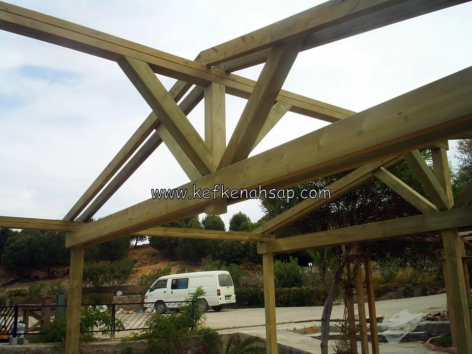 Pergola çatı kirişleri ve köşelerdeki çapraz payandalar, arkada otopark ve beyaz bir araç
