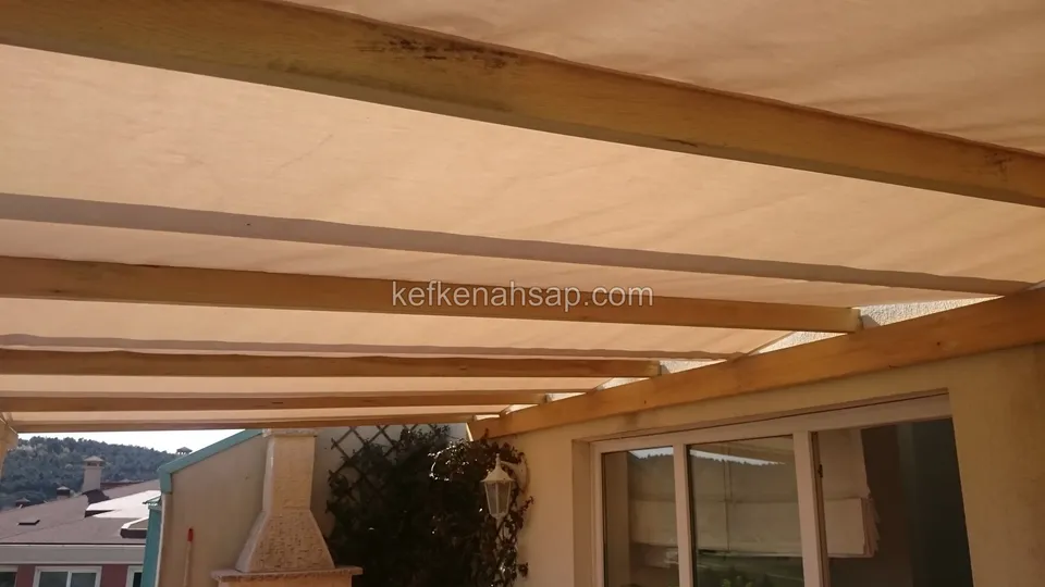 Ahşap pergola üzerine gerilmiş bej kumaş örtü, altında cam kapılı teras, kenarda kafes panel