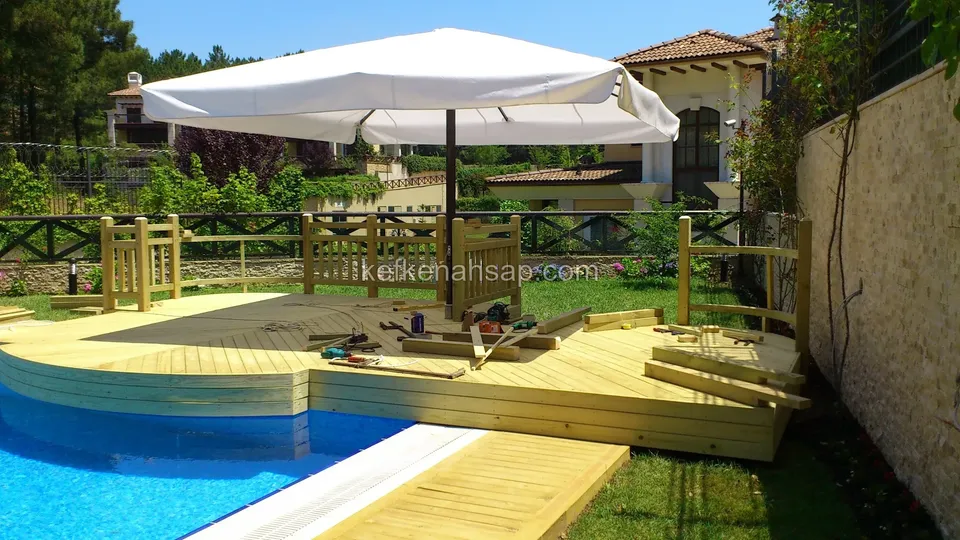 Timber railing being installed on the raised platform at the pool edge, with offcuts and hand tools lying on the deck
