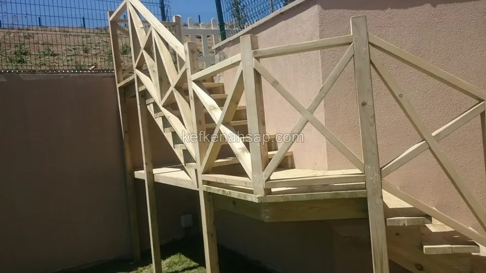 Pembe duvar önünde platform ve çaprazlı korkuluk; arkada yukarı çıkan merdiven ve tel çit