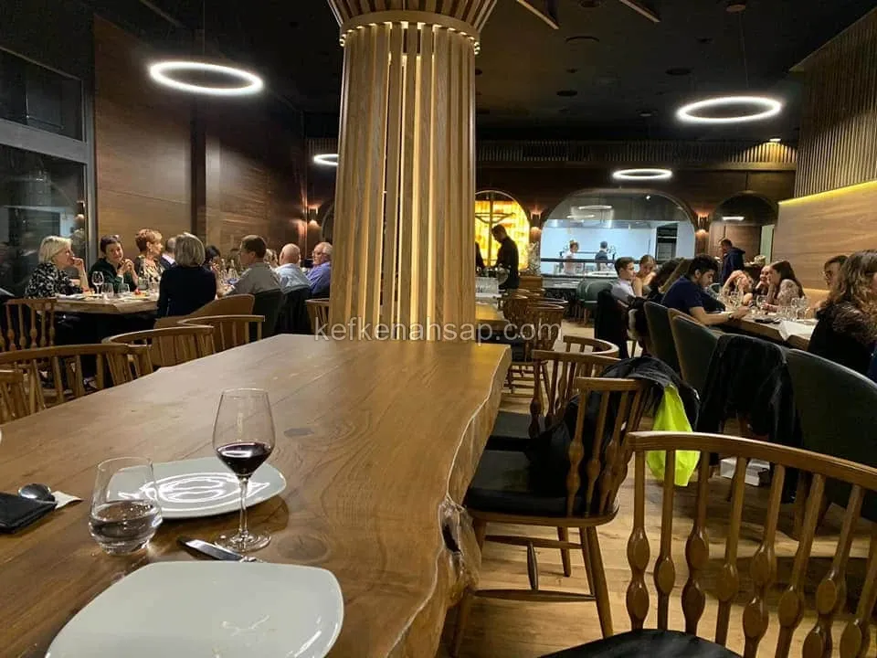 Massivholztisch mit natürlicher Kante, Holzstühle und mit senkrechten Latten verkleidete Säule im Restaurant.