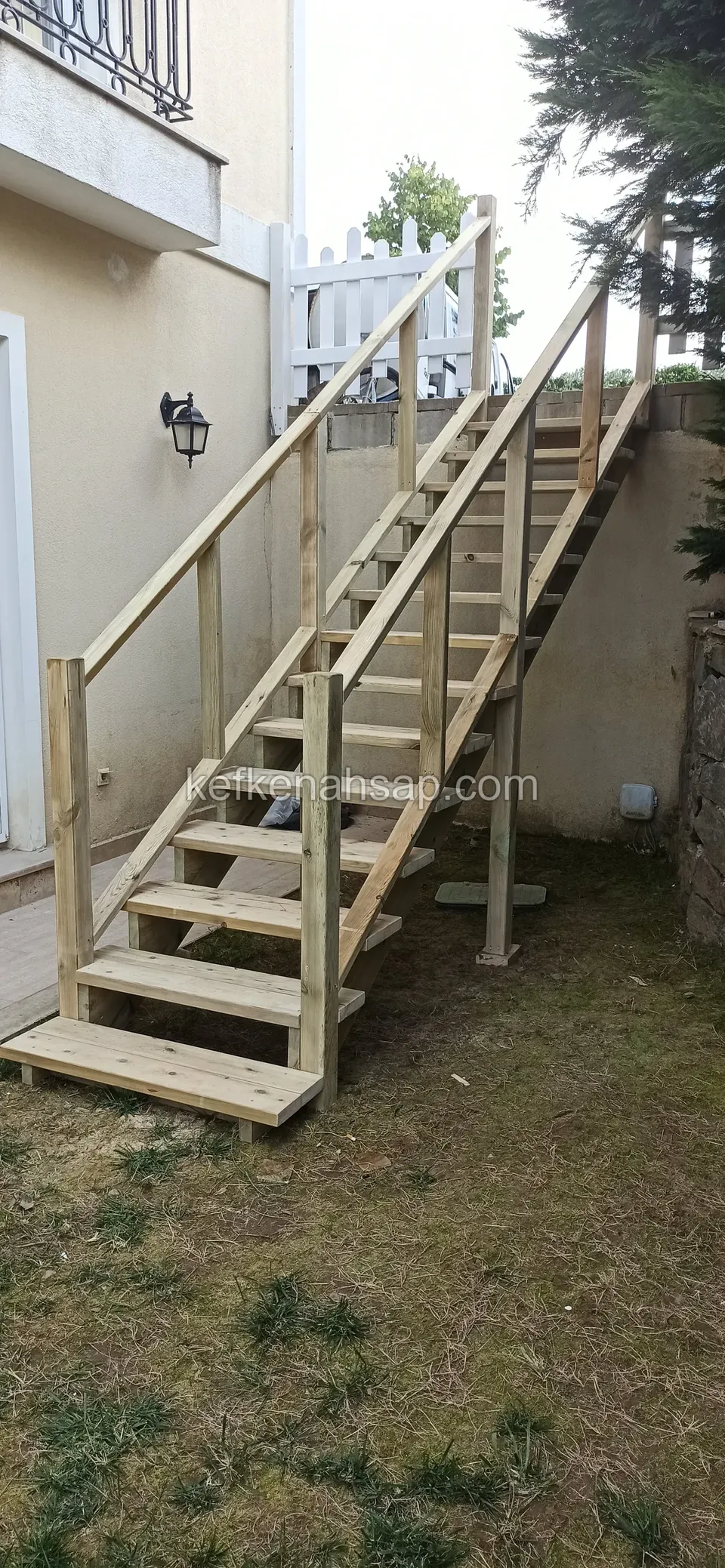 Holztreppe mit schlichtem Handlauf, die an der Hauswand zu einem weißen Zaun hin ansteigt