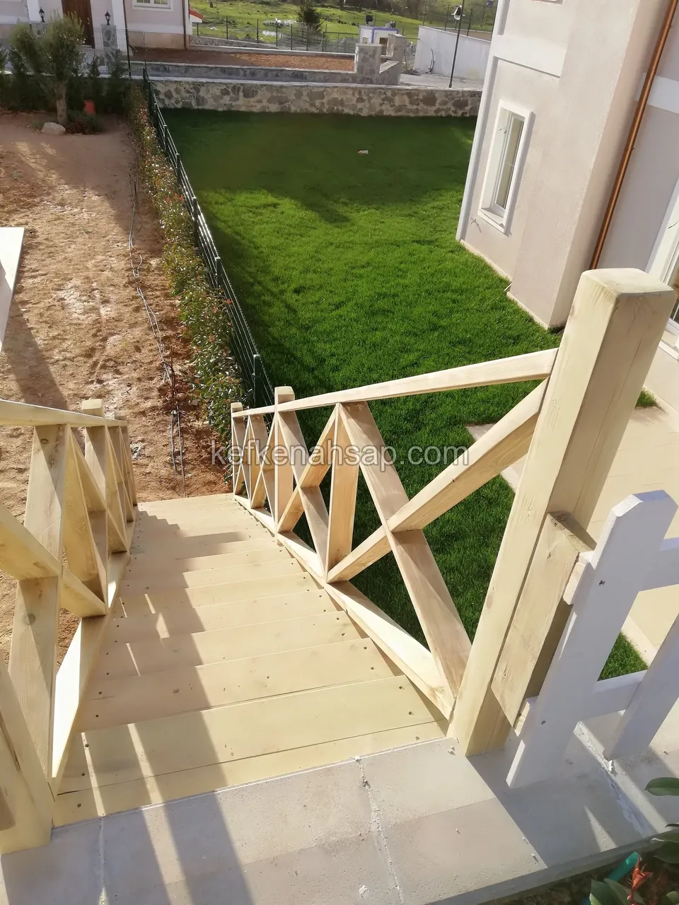 Blick von oben auf ein Holzpodest mit Kreuzstreben-Geländer und den Rasen darunter, seitlich die Hausfassade