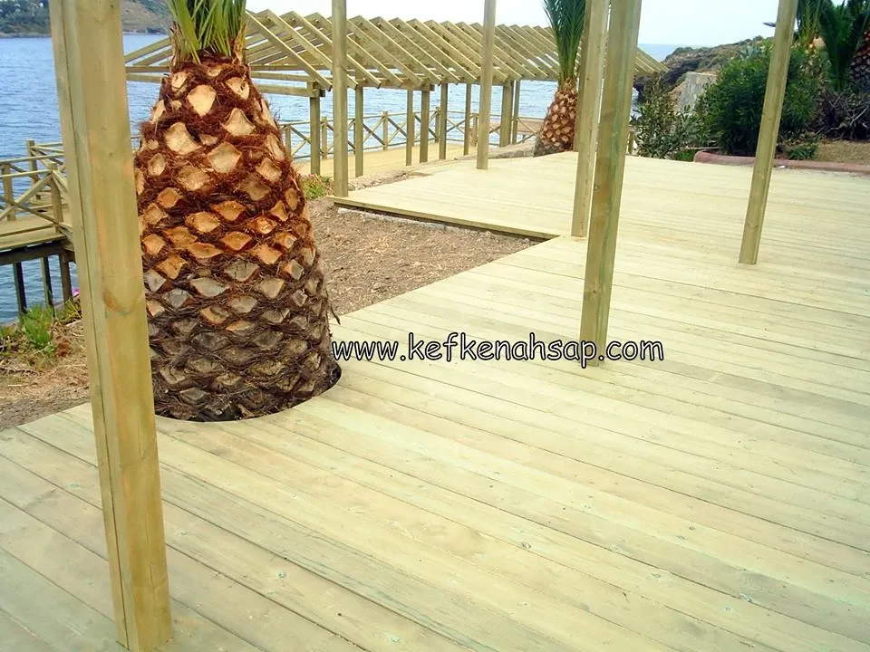 Deniz kenarında palmiye ağacı etrafına döşenmiş emprenyeli ahşap deck kaplama ve pergola dikmeleri.