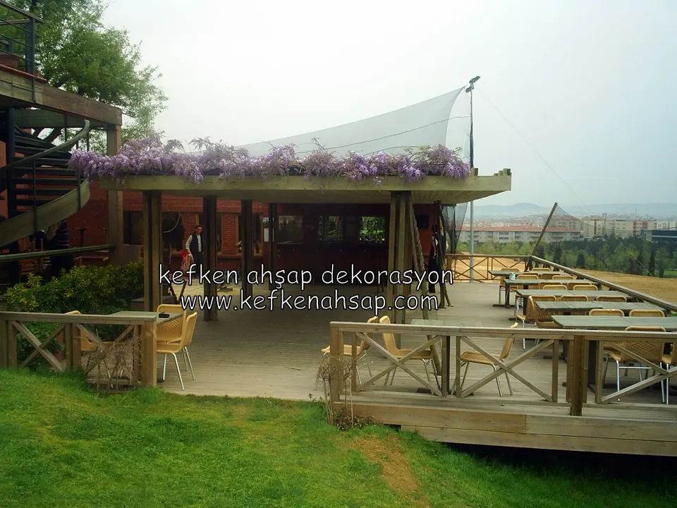 Salkımlı pergola altında ahşap deck, çapraz korkuluk, restoran masaları, spiral merdiven ve çimlik