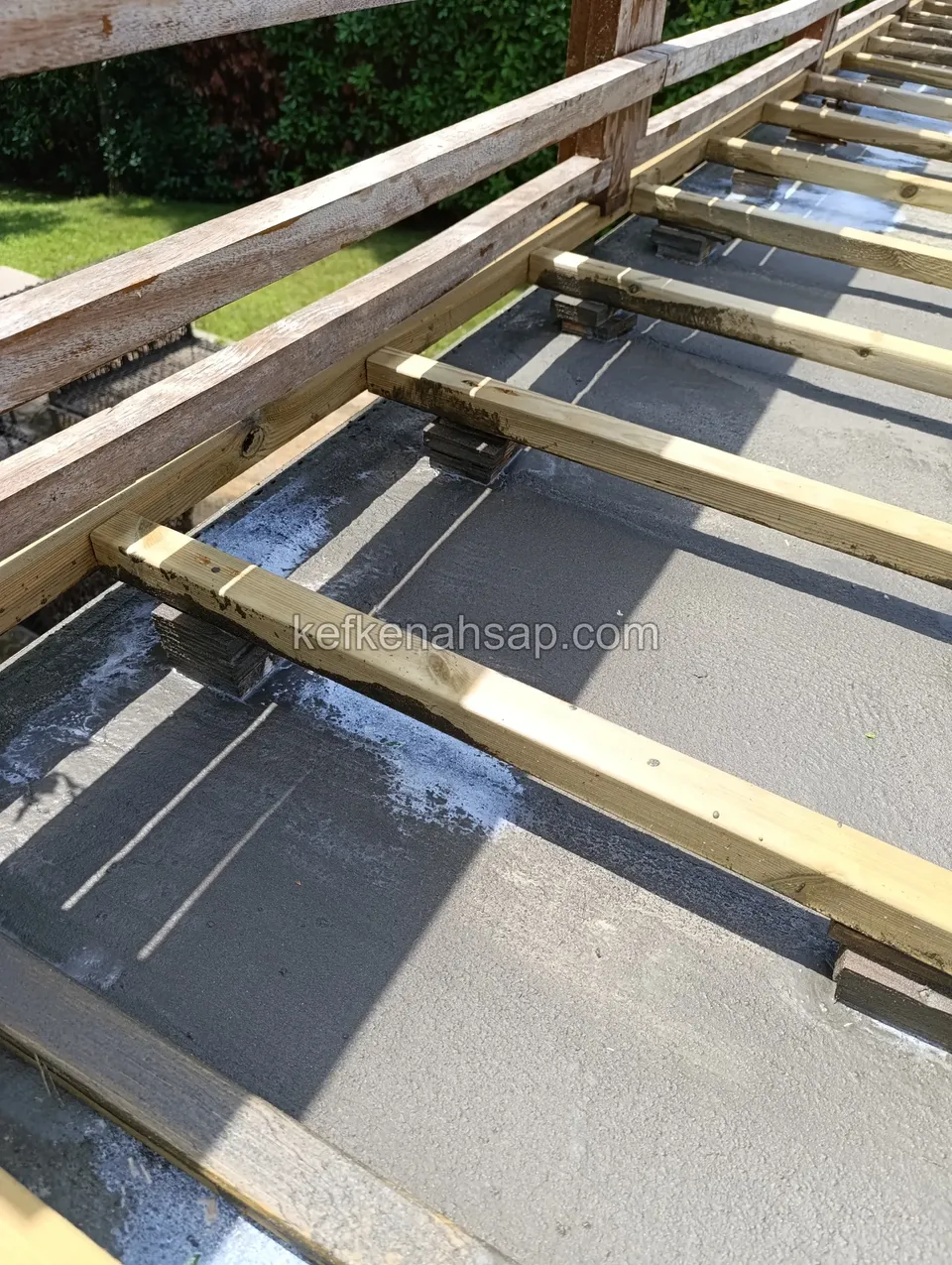 Pressure-treated battens set on pedestals over grey screed with a timber railing above, seen up close