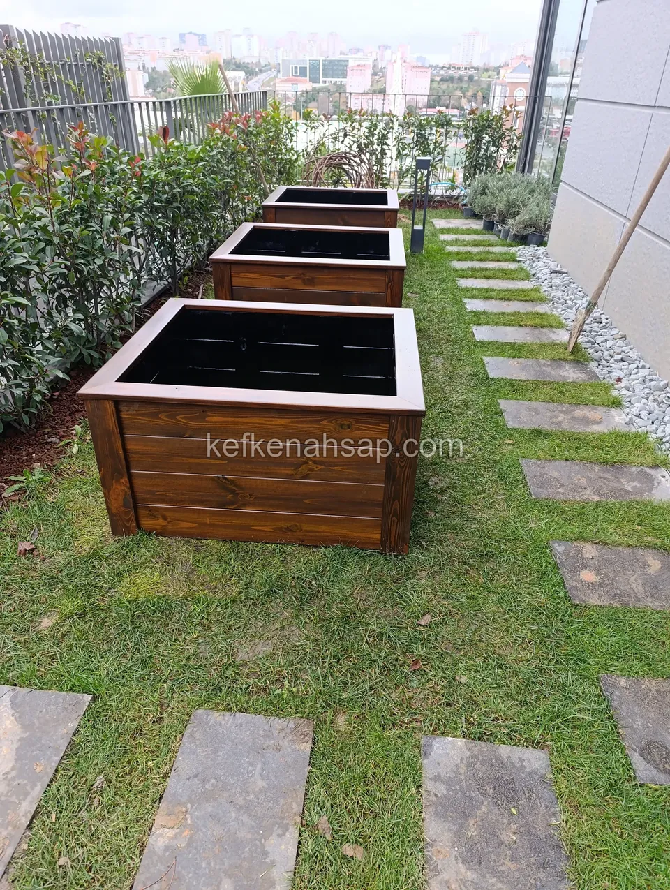 Dark-toned square timber planters lined up beside a stepping-stone path on a lawn