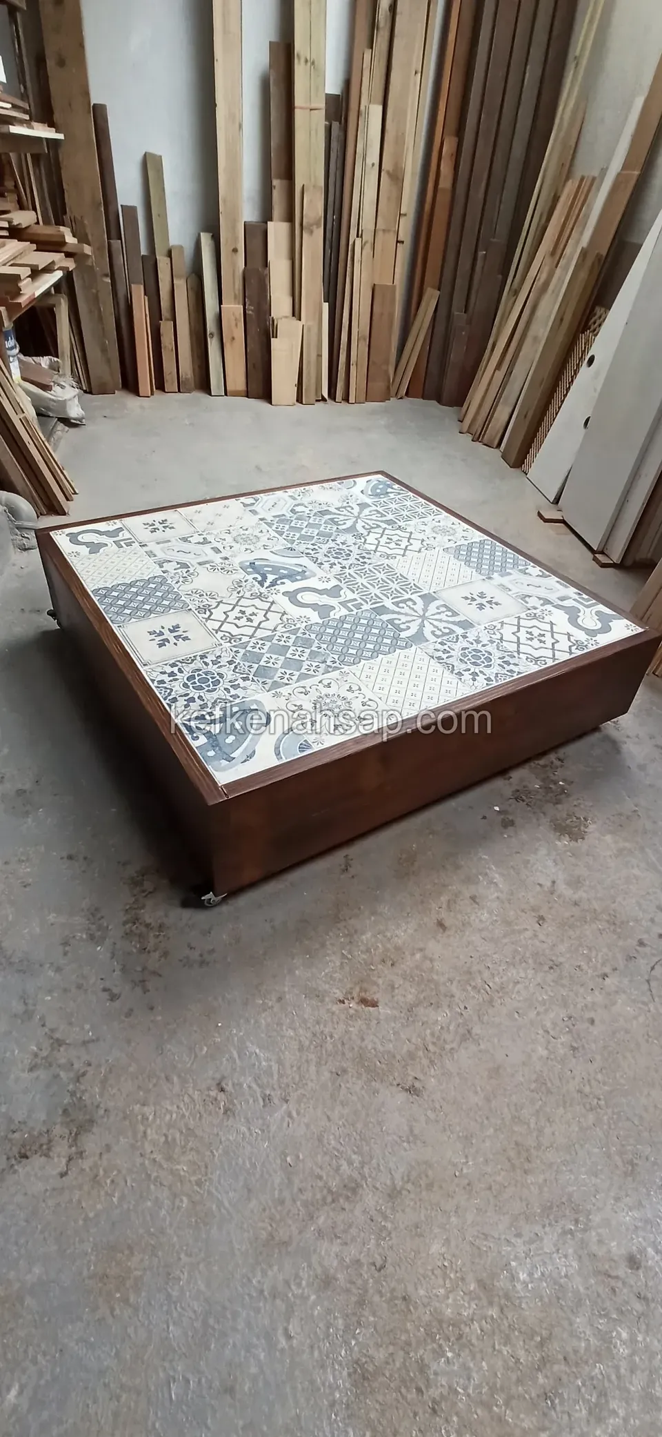 Ein niedriger Holztisch mit blau-weißer Keramikplatte auf dem Betonboden einer Werkstatt
