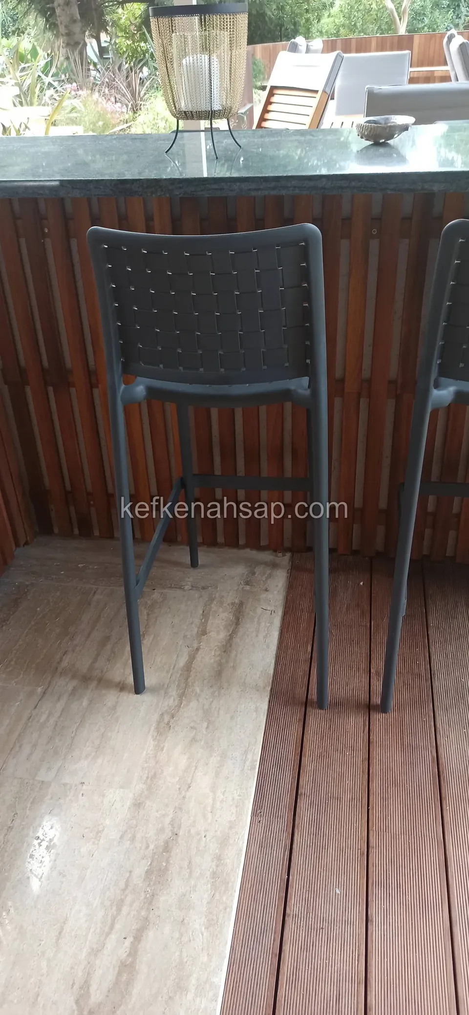 Ahşap şeritlerle kaplı bar tezgahı, iki yüksek taburesi ve deck zeminin traverten zemine geçtiği yer, yakın çekim