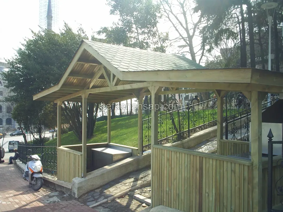 Açık renk ahşap kamelya, shingle çatı, alt kısmı tahta korkuluklu; yanında bir motosiklet park etmiş