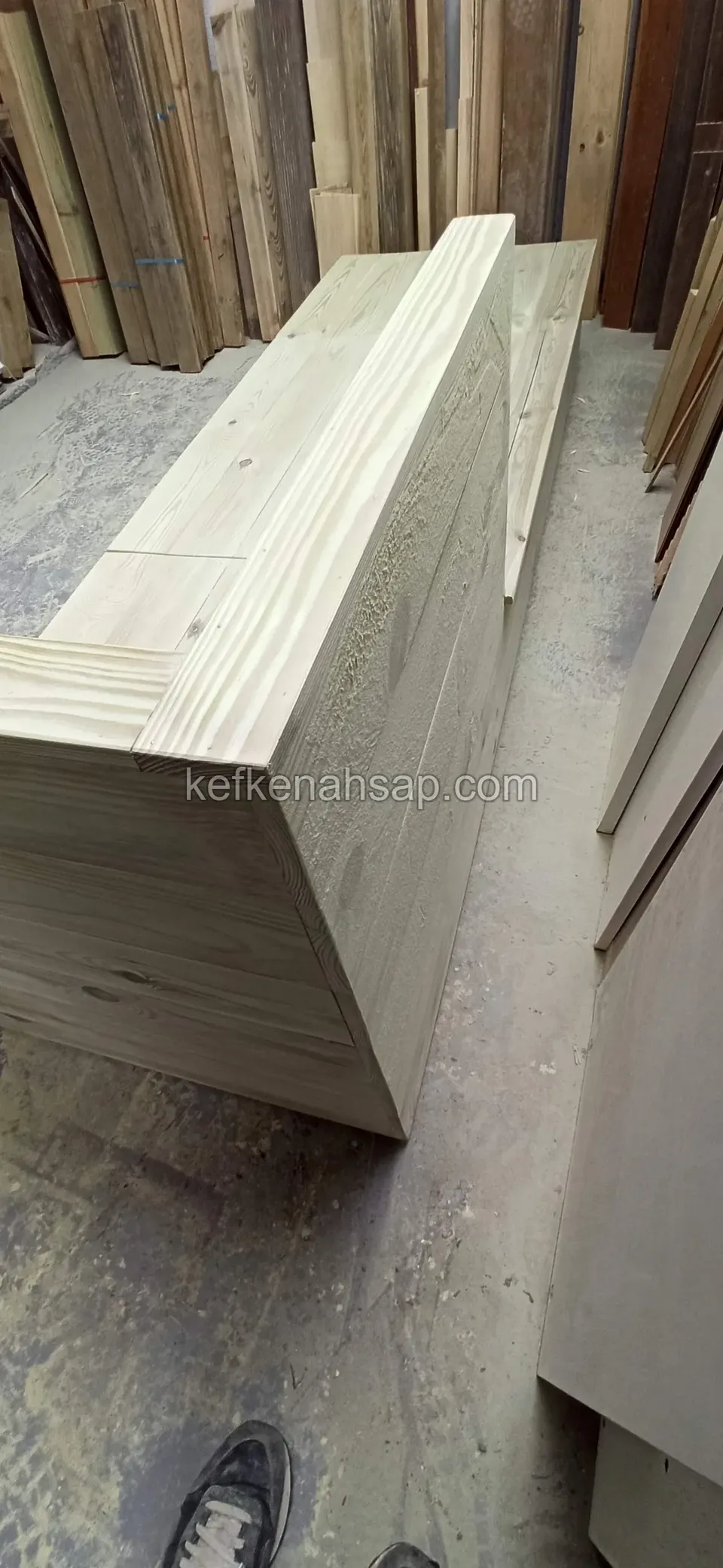 Seitenansicht einer Holzbank in der Werkstatt neben Schnittholz, die Oberseite von einer dicken Kante eingefasst