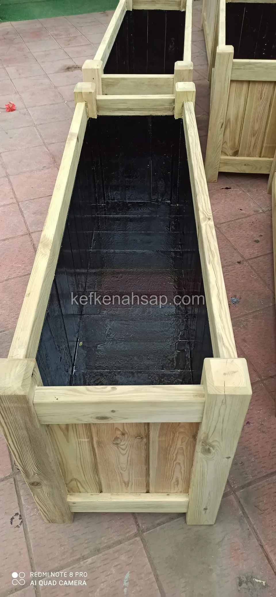 Long light timber planter with a black liner on a tiled floor and a second one beside it