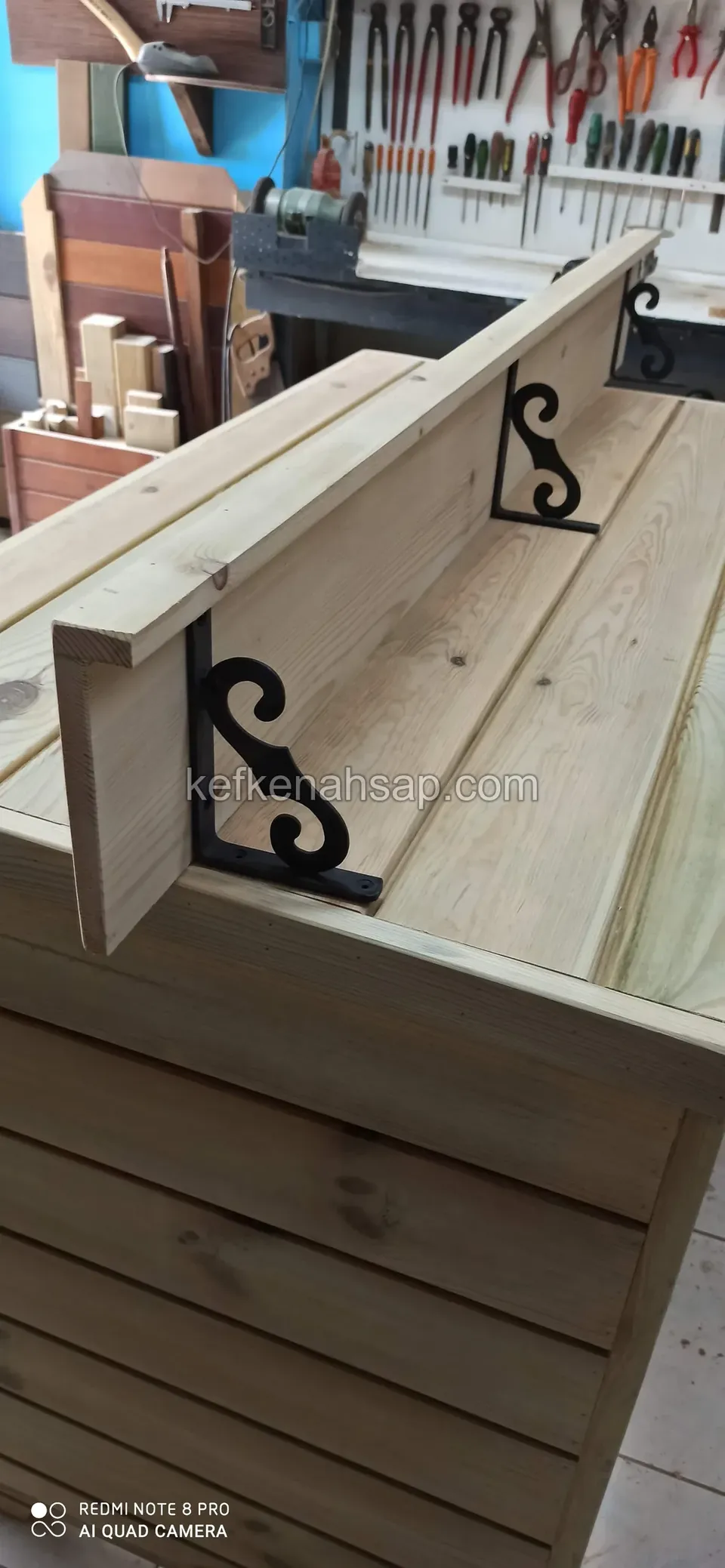 Nahaufnahme eines hellen Regalbretts, das mit schwarzen verzierten Gusskonsolen an einer Holzfläche montiert ist
