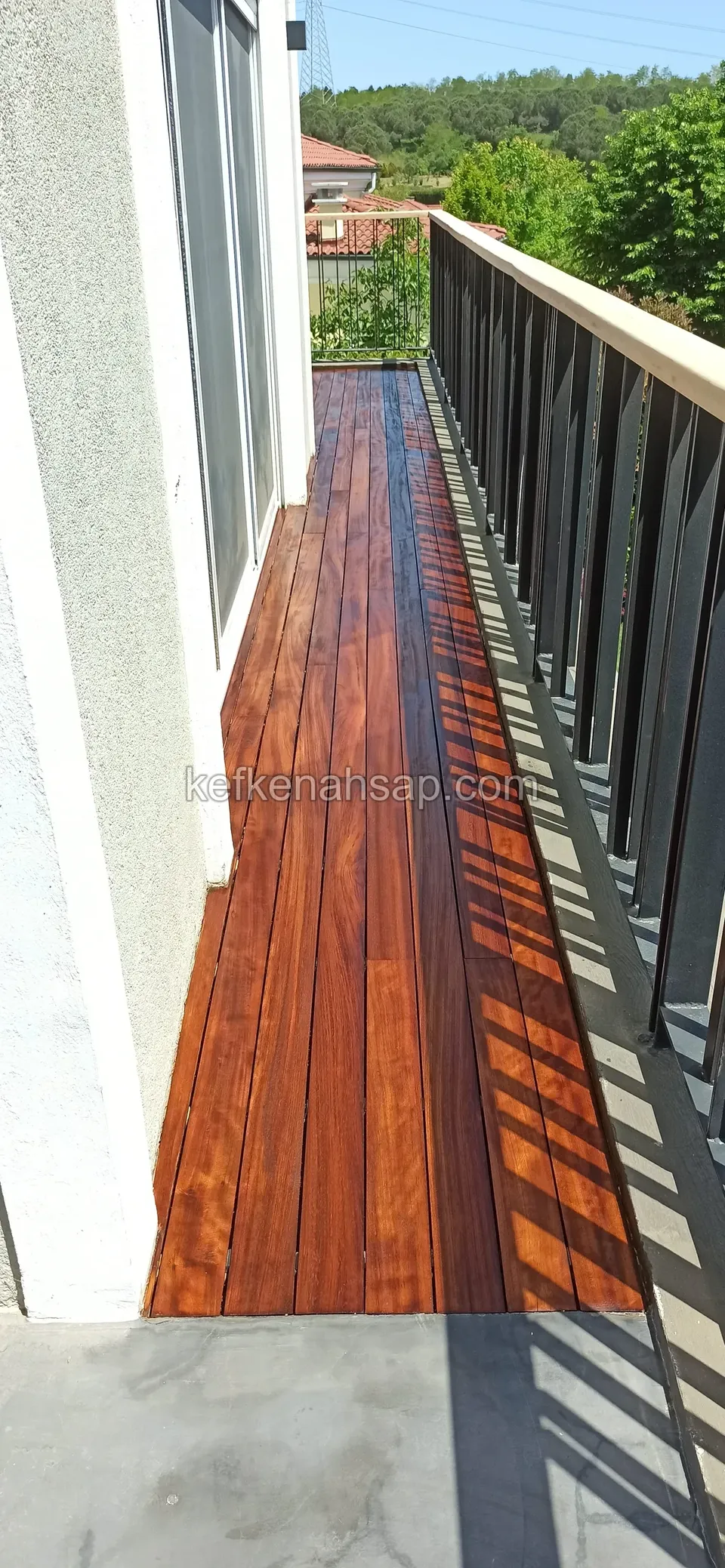 Glossy red-brown deck covering a long narrow balcony from end to end, with a black metal railing beside it