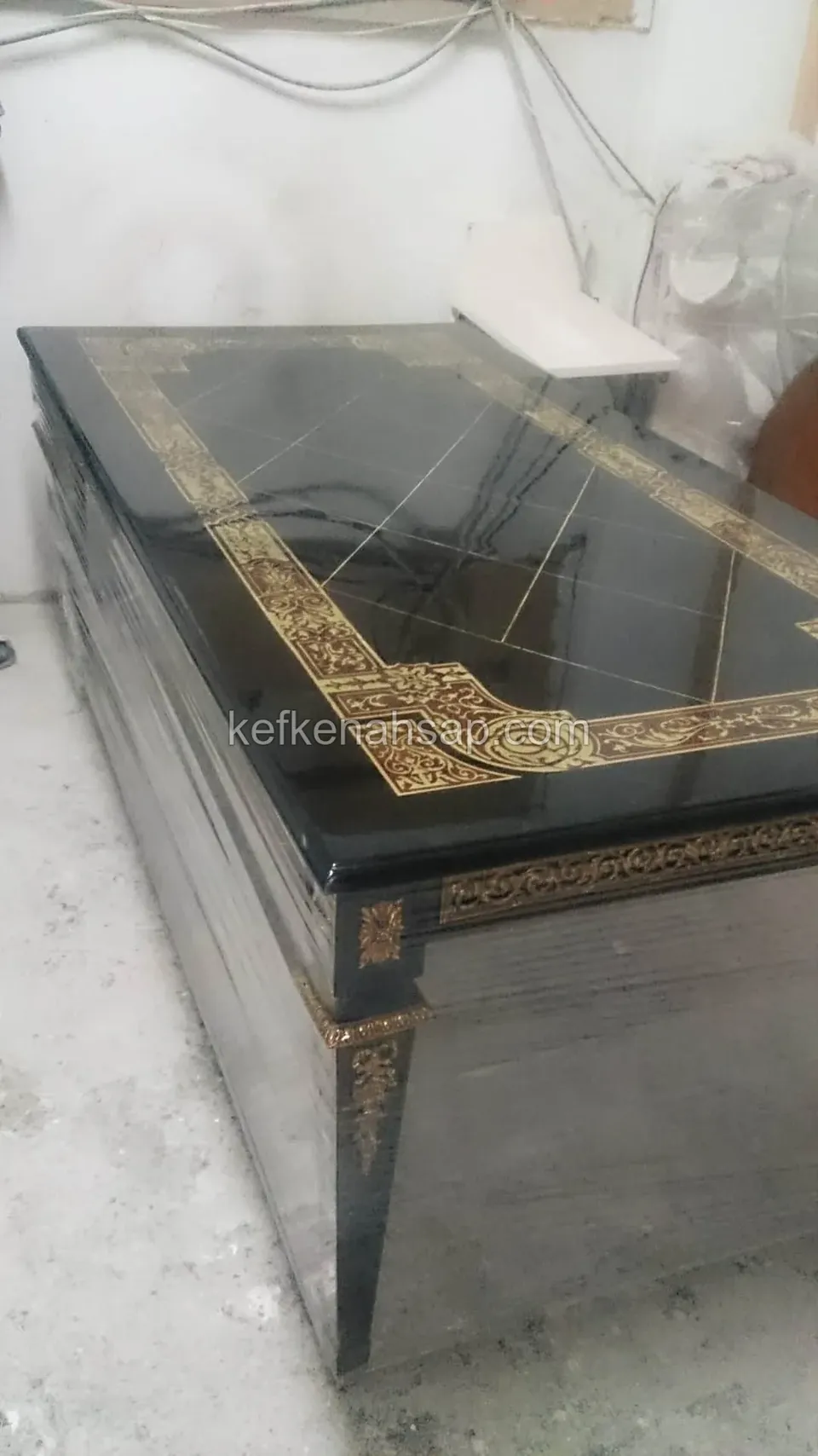 Siyah parlak cilalı dikdörtgen masa; üst yüzeyde ve kenarlarda altın renkli süslemeli bordür deseni var