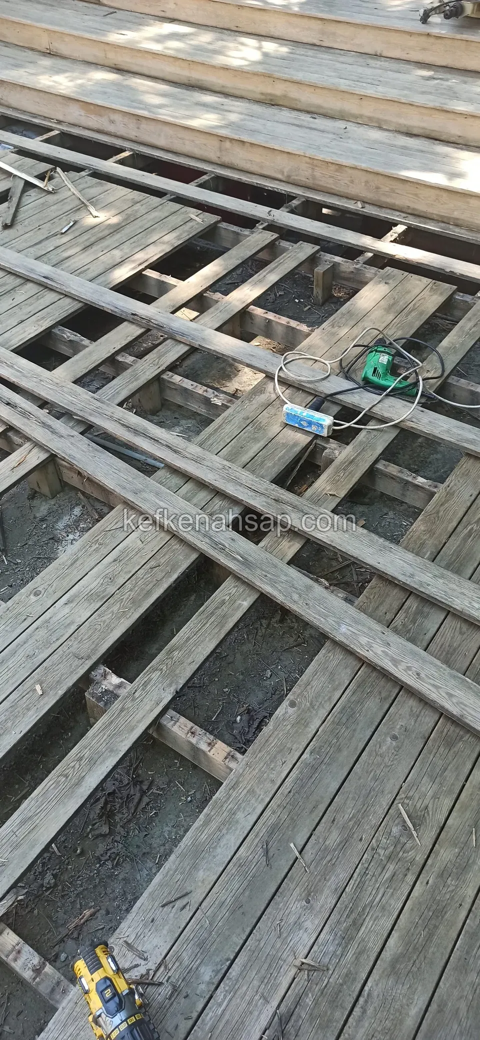 Joists exposed where an old grey deck has been taken up, with a drill and a batten on the ground