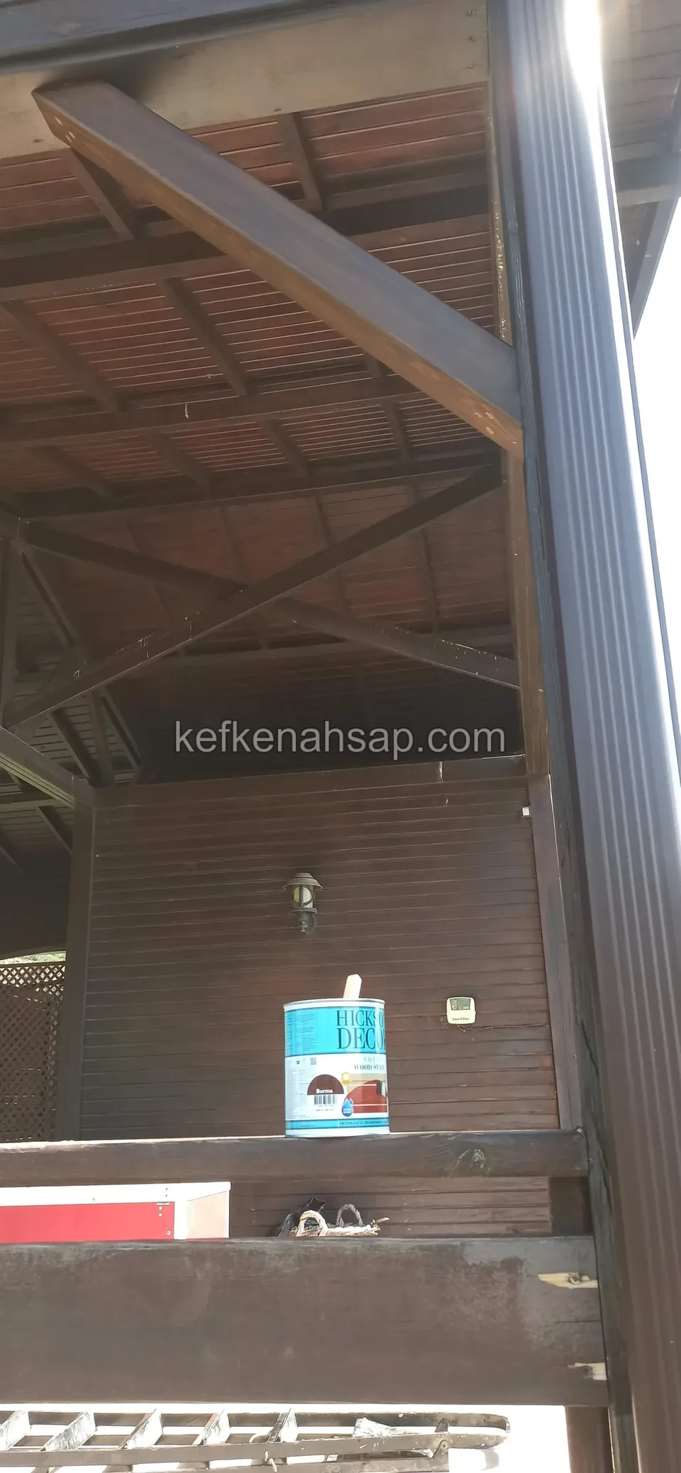 Sundurma kolonu, eğik destek ve ahşap çatı altı; arkada ahşap kaplı duvar görünüyor