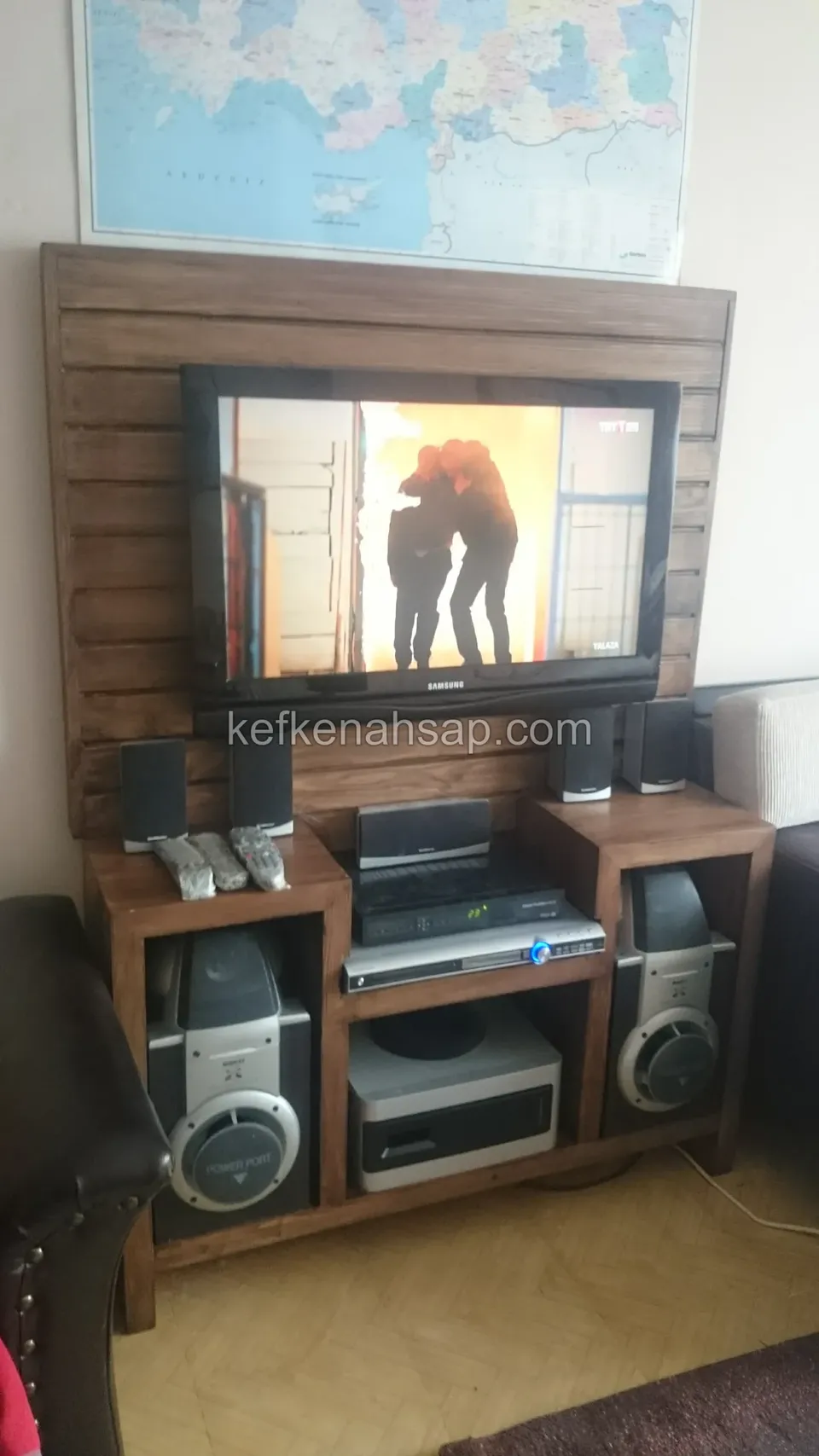 Yatay tahta panel arkalıklı ahşap TV ünitesi; iki yanda hoparlör gözleri, ortada cihaz rafı