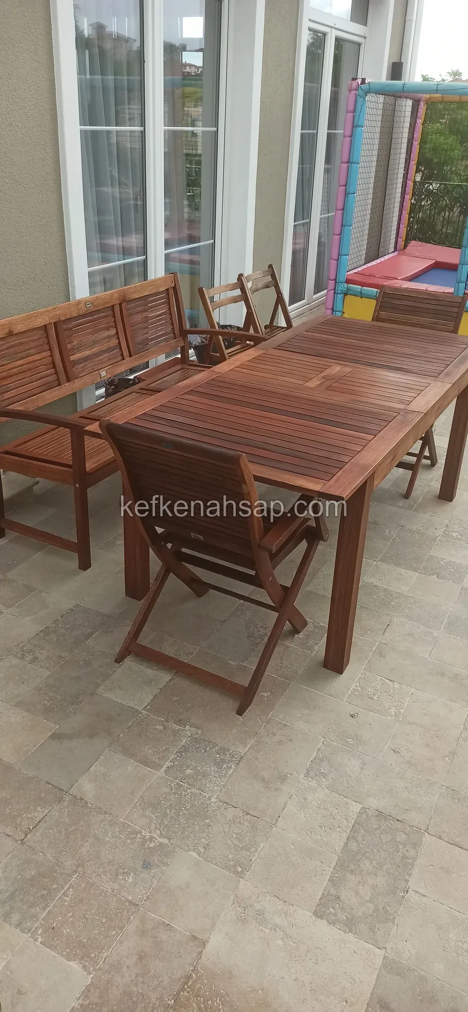 Taş döşemeli teraste açılır ahşap masa, katlanır sandalye ve kanepe