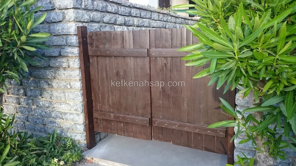 Taş duvarlar arasındaki girişte, yatay kuşakları olan koyu kahve dikey tahtalı ahşap çift kanatlı kapı
