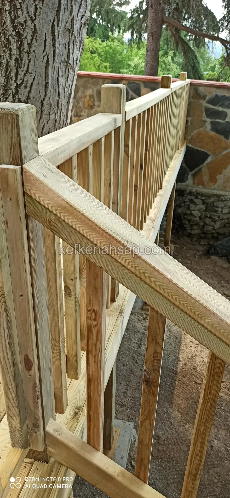 درابزين خشبي بمسند يد يبدأ بجانب جذع شجرة ويمتد على طول جدار حجري