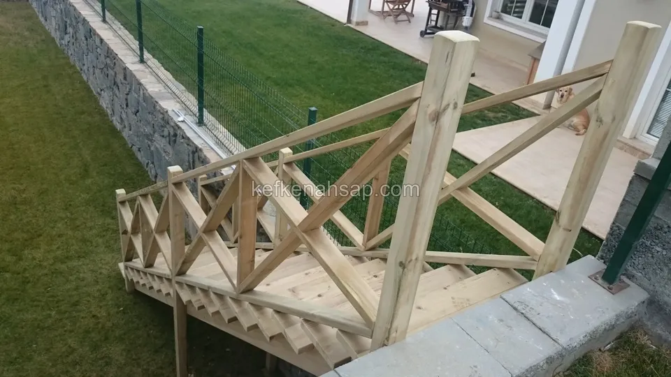 Çimenliğe inen çapraz korkuluklu ahşap merdiven, solda taş duvar ve tel çit