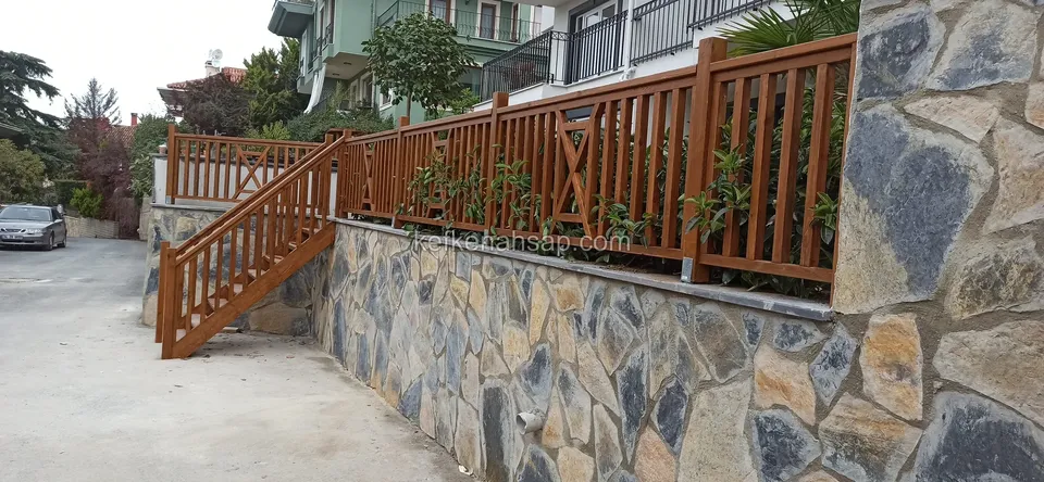 Taş kaplı istinat duvarının üstünde ve yanındaki merdivende devam eden kahverengi tonlu ahşap korkuluk
