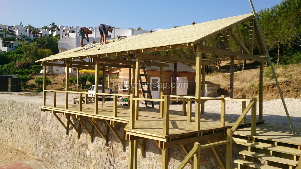 Taş duvarın üstünde konsol payandalarla yükseltilmiş deck ve kamelya, çatıda iki usta çalışıyor