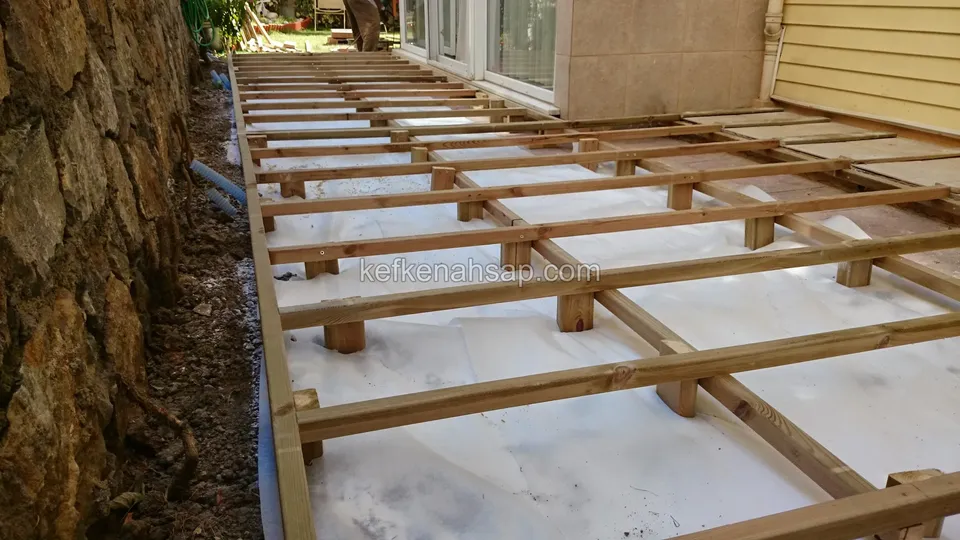 إطار عوارض مقام بجانب جدار استنادي حجري ومنزل وقد بدأ تركيب ألواح الديكينغ على اليمين