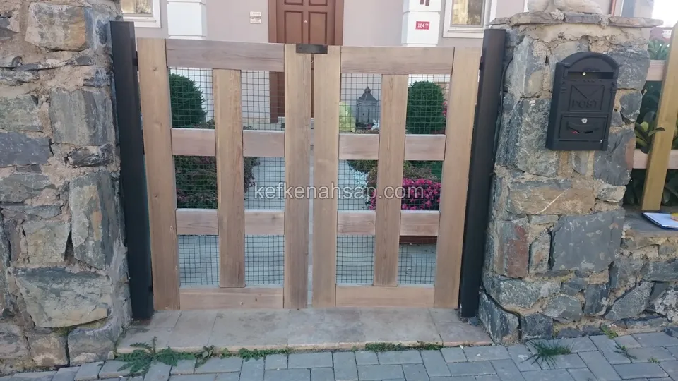 Taş kolonlar arasında ahşap çerçeveli ve tel örgülü iki kanatlı bahçe kapısı