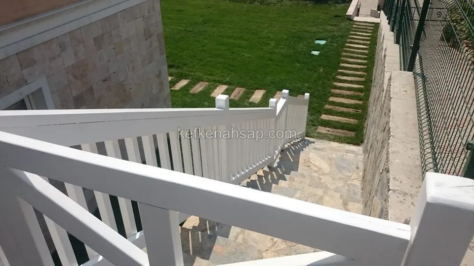 Köşeden bakışla taş merdivenin yanındaki beyaz boyalı korkuluk; üstte bir bölüm daha, yanda çimlik ve tel çit