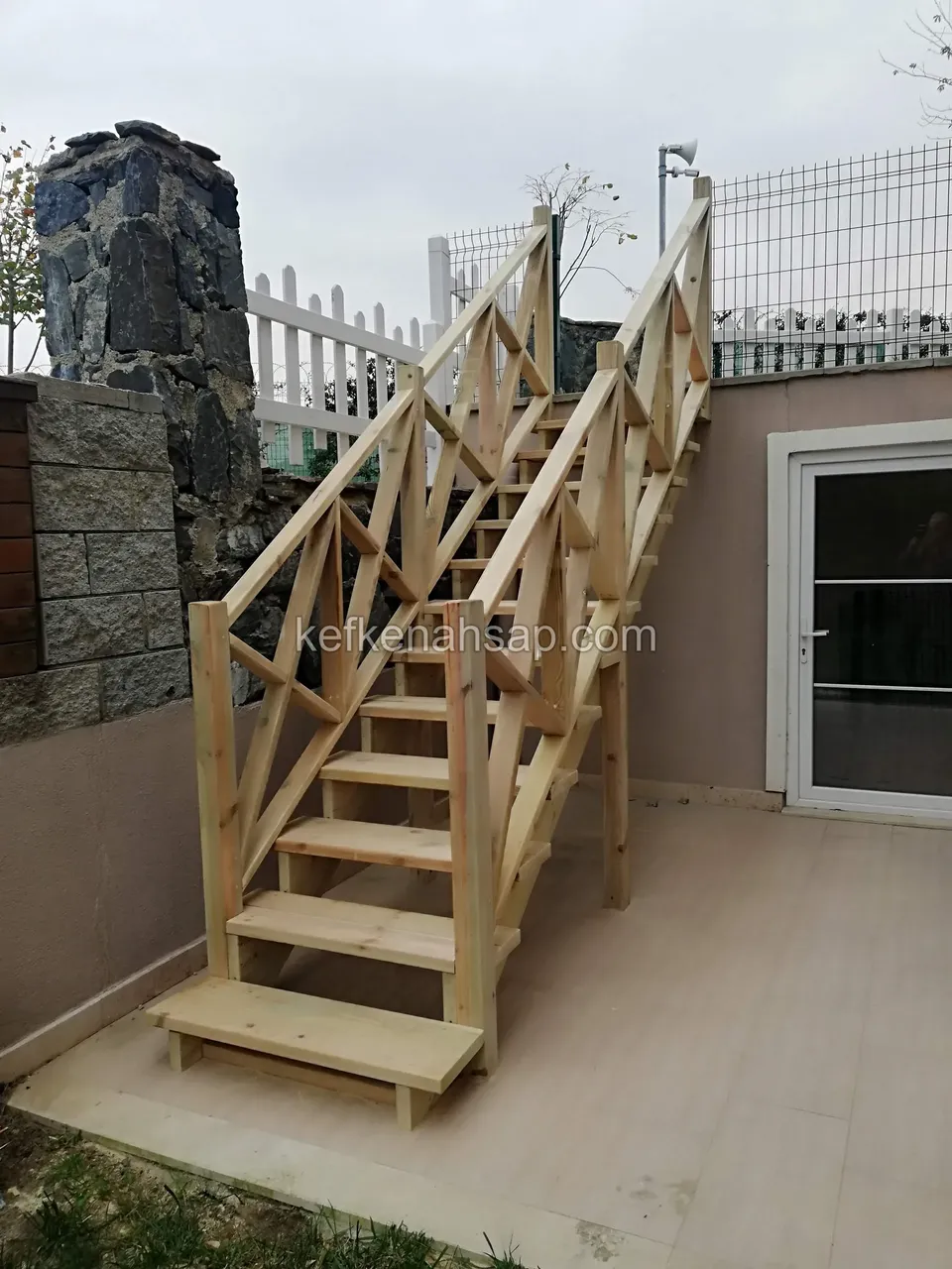 Holztreppe mit Diagonalgeländer im gefliesten Hof zwischen Steinsäule und Glastür