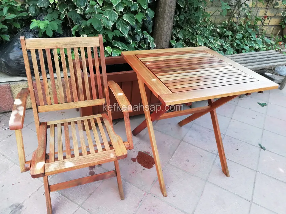 On stone paving, a timber armchair with a tall slatted back and a small square folding table beside it, with ivy behind