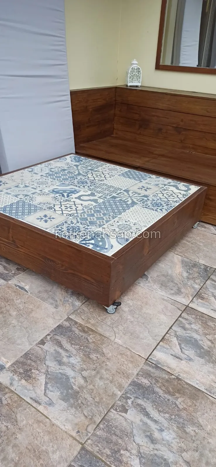Low wooden table on wheels with a blue and white patterned tile top, in front of a dark wood built-in corner bench