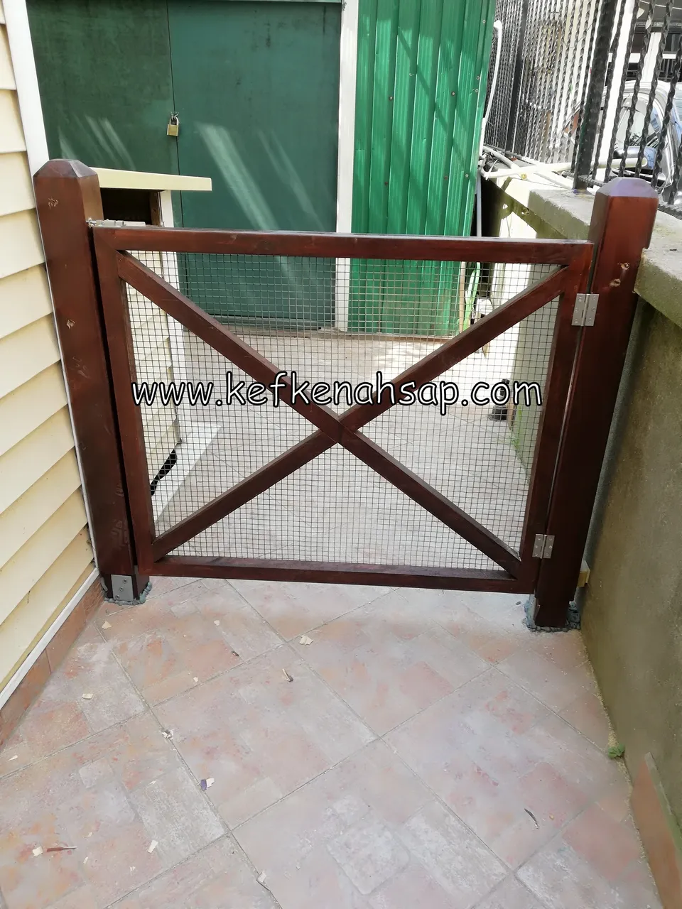 Dark stained wooden gate with X-brace design and wire mesh installed in an outdoor walkway.