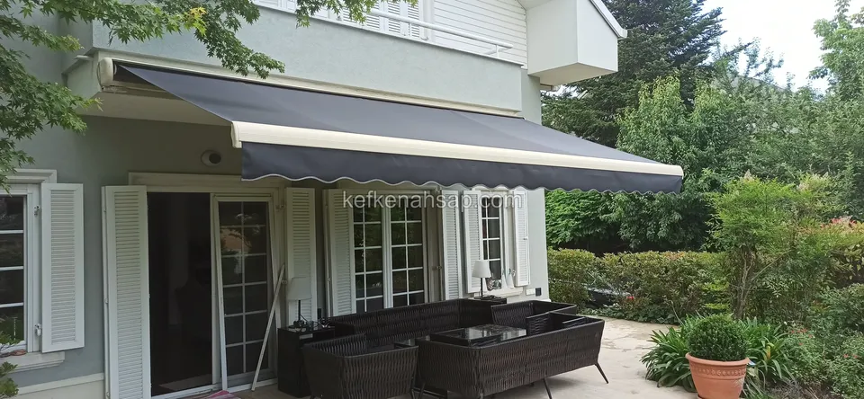 Ein dunkles Sofaset in Rattanoptik steht im Schatten einer Markise vor den Glastüren eines Hauses