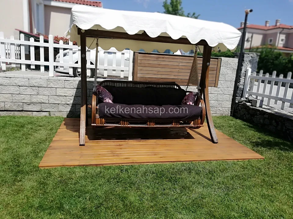 Çimin üzerine serilmiş ahşap deck zeminde, krem tenteli üç kişilik ahşap bahçe salıncağı
