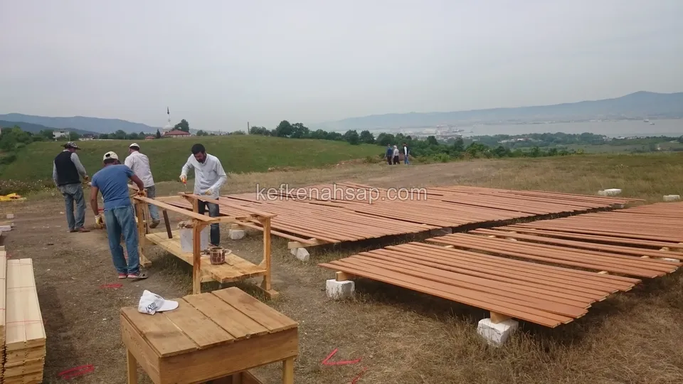 На открытом холме с видом на море панели террасы разложены на земле рядом с рабочими столами, над ними работают три человека