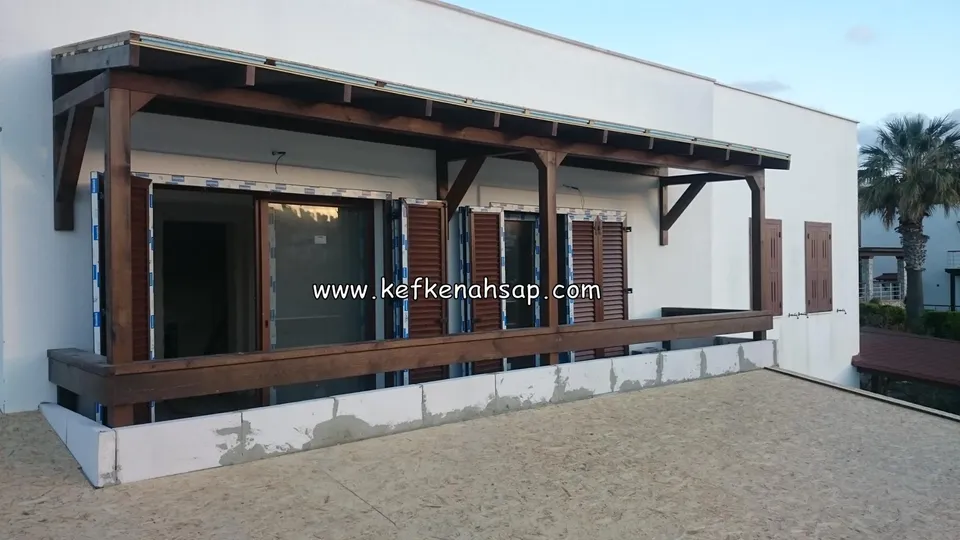 Beyaz cepheli binanın terasında koyu renkli ahşap pergola sundurması ve korkuluğu.