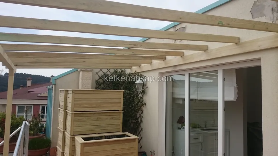 Cam sürgülü teras kapısının önünde pergola kirişleri, kafes panel ve üst üste ahşap saksılıklar