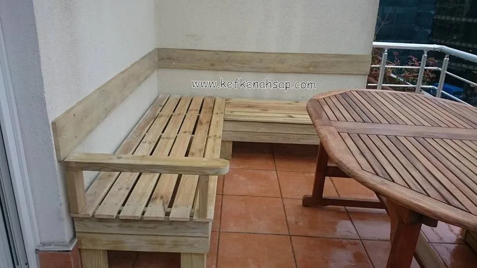 L-shaped slatted wooden bench with an armrest against a terrace wall, next to a wooden dining table.