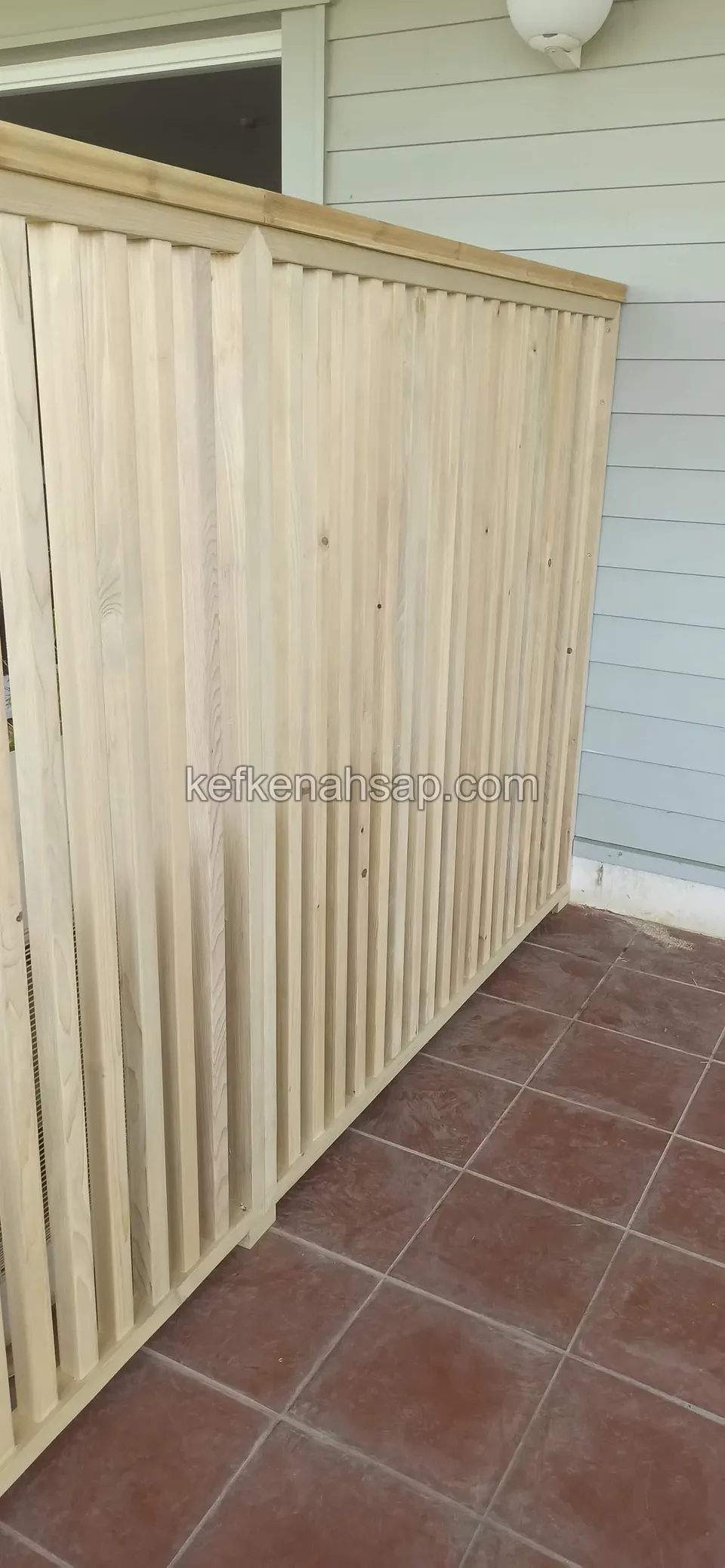 Tall pale timber screen of vertical slats in a terrace corner with red tiles, with a grey timber-clad facade behind