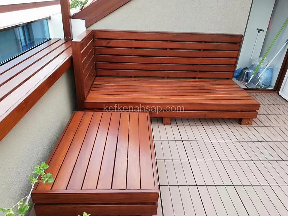 Reddish-brown L-shaped wooden bench with slatted backrest in a terrace corner, with a low wooden ottoman in front