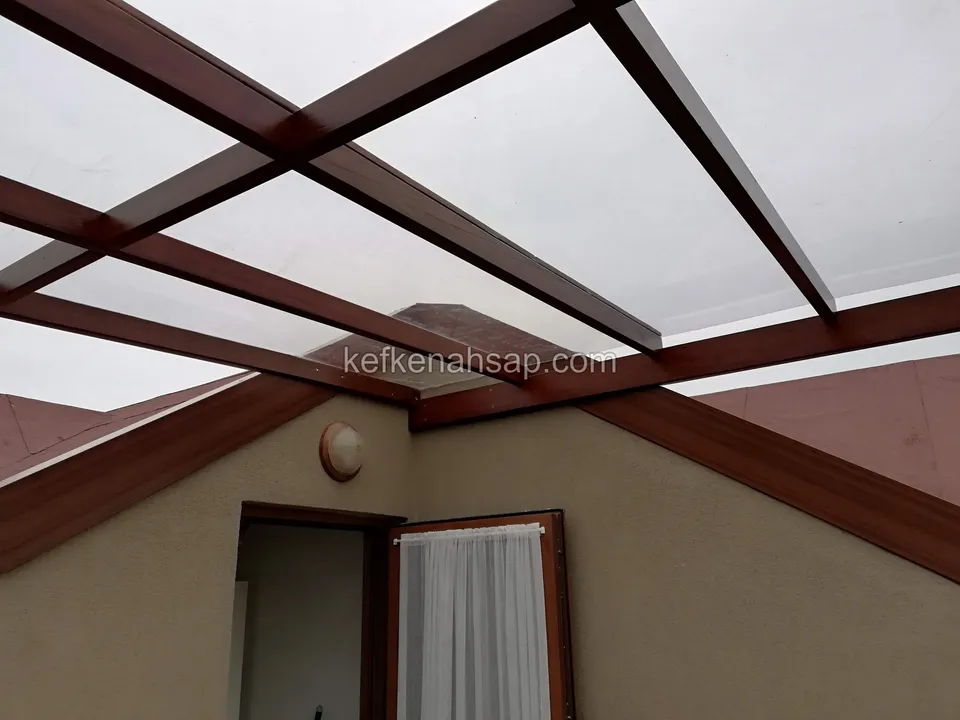Crossing dark red varnished beams with a clear roof sheet over a terrace, with an attic door at the side
