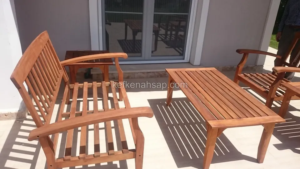 Auf einem hellen Terrassenboden vor einem Haus mit Glastüren stehen eine Lattenbank aus Holz