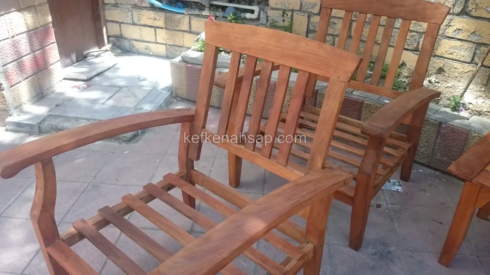 Taş duvarın önündeki teraste, çıtalı oturaklı iki kollu ahşap koltuk