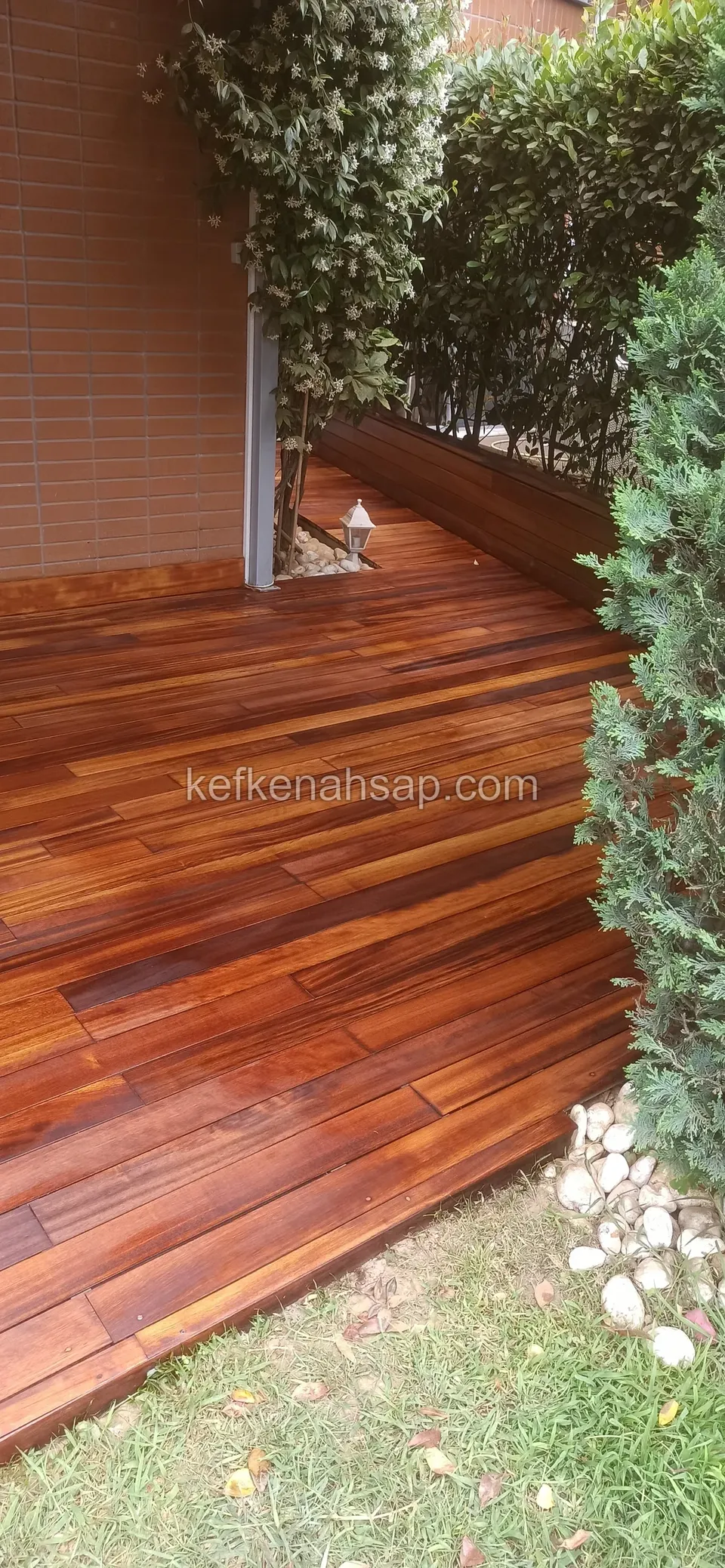 Glossy dark-toned timber deck at the foot of a brick-clad wall, framed by plants