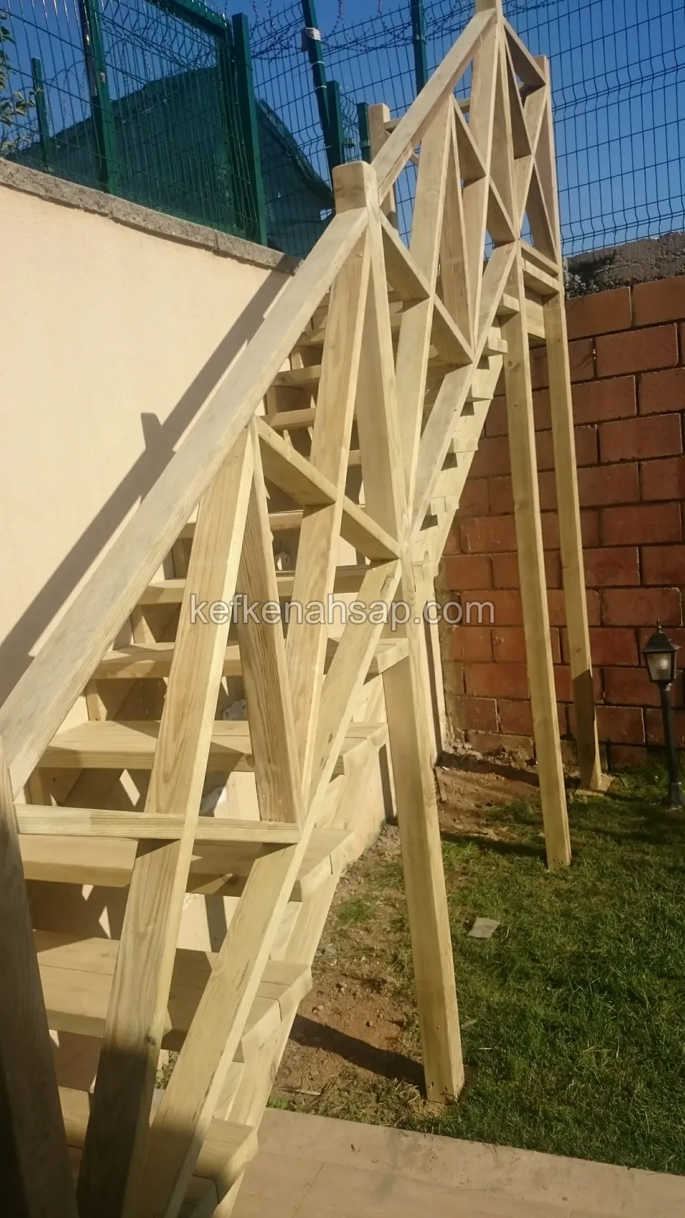 Helle Holztreppe mit Kreuzstreben-Geländer, die neben einer Wand aus Backstein und Putz aufsteigt